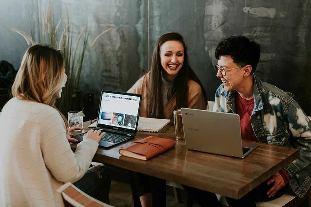 Group of people smiling and using laptops at a table.
